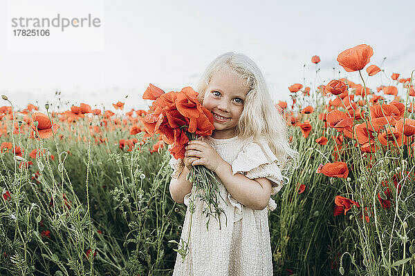Lächelndes Mädchen mit roter Blume im Mohnfeld