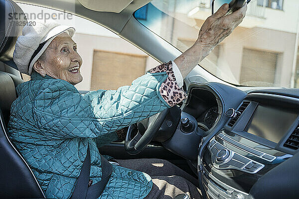 Glückliche ältere Frau  die den Rückspiegel im Auto einstellt