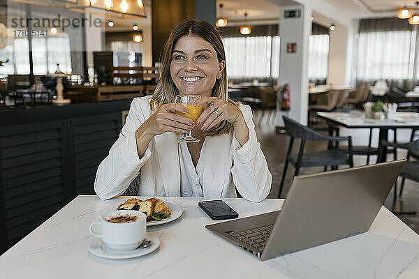 Lächelnde Geschäftsfrau mit Saftglas und Laptop im Restaurant