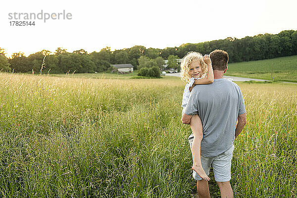 Vater trägt lächelnde Tochter auf dem Feld