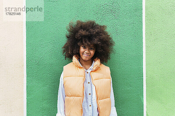 Smiling girl with Afro hairstyle standing in front of green wall