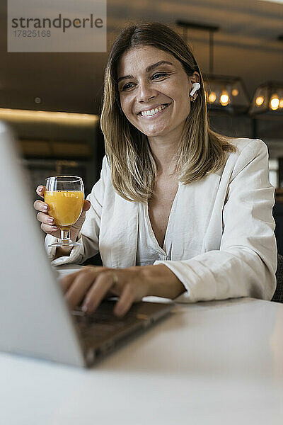 Lächelnde Geschäftsfrau hält Saftglas mit Laptop im Restaurant
