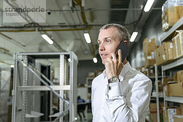 Geschäftsmann spricht in Fabrik mit Smartphone