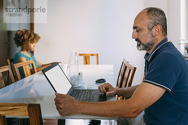 Mann benutzt Laptop und sitzt mit Tochter am Tisch