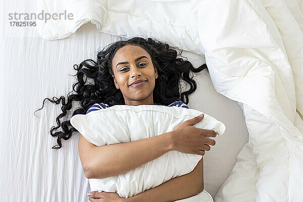 Happy woman embracing cushion on bed at home