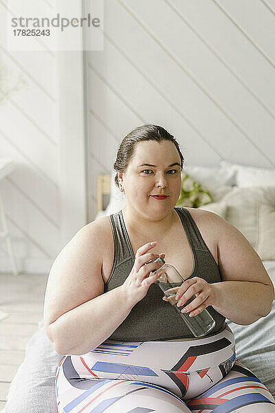 Frau mit Wasserflasche sitzt zu Hause im Bett