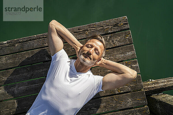 Lächelnder reifer Mann entspannt sich am Pier über dem See