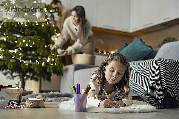 Mädchen schreibt Brief an den Weihnachtsmann  Eltern im Hintergrund zu Hause