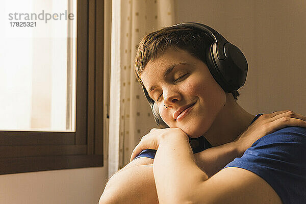 Smiling woman with eyes closed listening music through wireless headphones at home