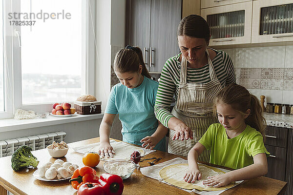Mutter hilft Töchtern bei der Pizzazubereitung in der heimischen Küche