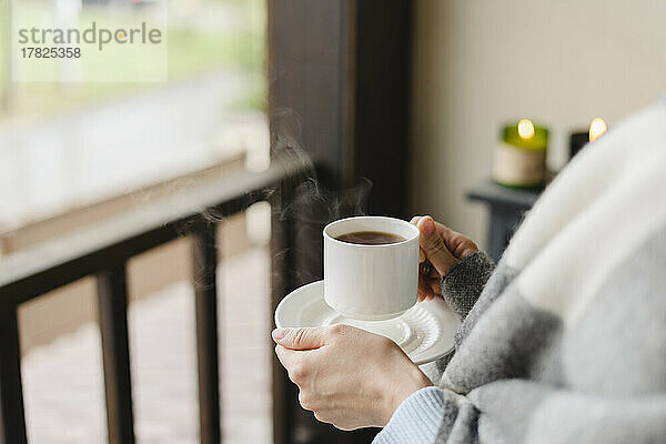 Hände einer Frau  die zu Hause Kaffeetasse und Untertasse hält