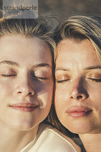 Mother and daughter with eyes closed on sunny day
