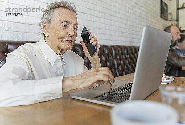 Ältere Frau mit Smartphone und Laptop im Café