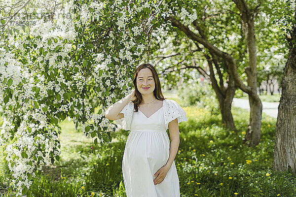 Lächelnde schwangere Frau steht im Park