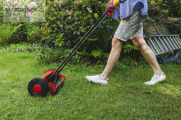 Frau mäht Rasen im Garten