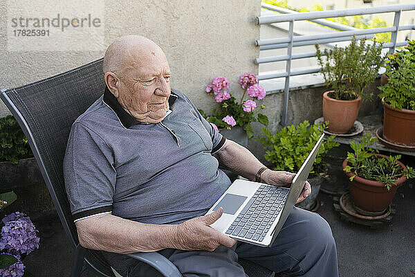 Älterer Mann mit Laptop sitzt auf Balkon