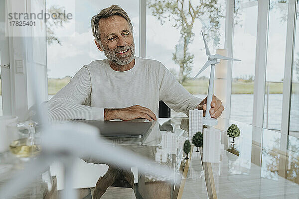 Glücklicher Mann mit Windturbinenmodell  der zu Hause sitzt