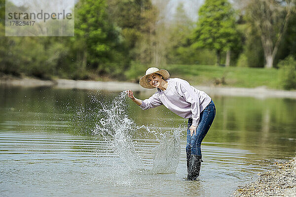 Glückliche Frau mit Hut  die Wasser am See spritzt