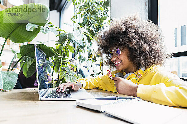 Glückliches Mädchen  das Laptop mit Süßigkeiten benutzt und im Café sitzt