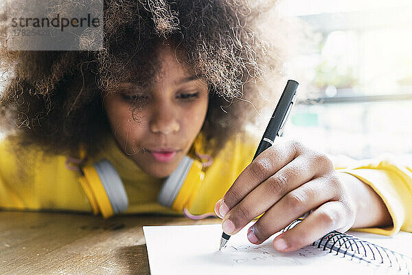 Mädchen schreibt mit Stift auf Notizbuch im Café