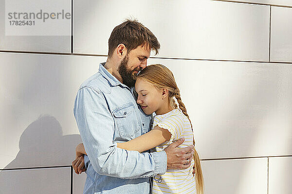 Smiling man embracing daughter in front of wall