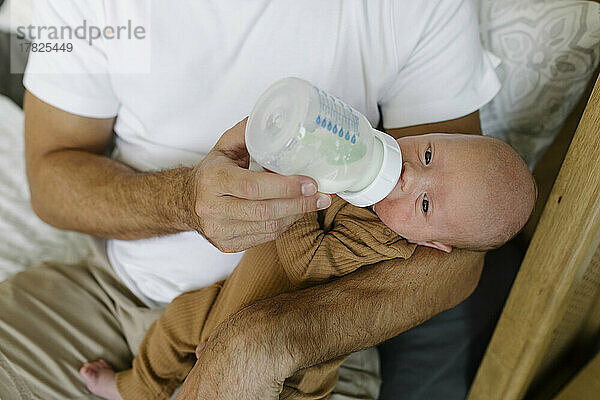 Mann füttert Baby zu Hause mit Flasche mit Milch