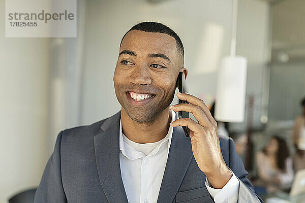 Glücklicher Geschäftsmann  der im Büro mit dem Mobiltelefon spricht