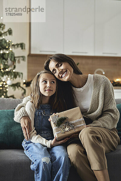 Glückliche Frau mit Weihnachtsgeschenk umarmt Tochter im Wohnzimmer