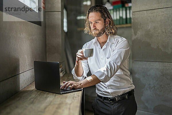 Seriöser Geschäftsmann trinkt Kaffee mit Laptop im Büro