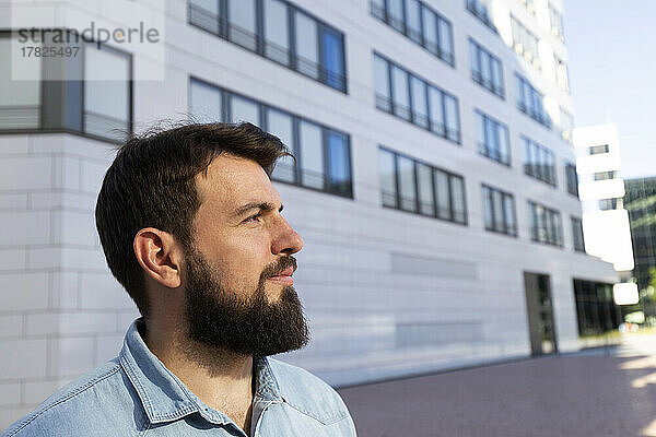 Lächelnder Mann mit Bart steht vor dem Gebäude