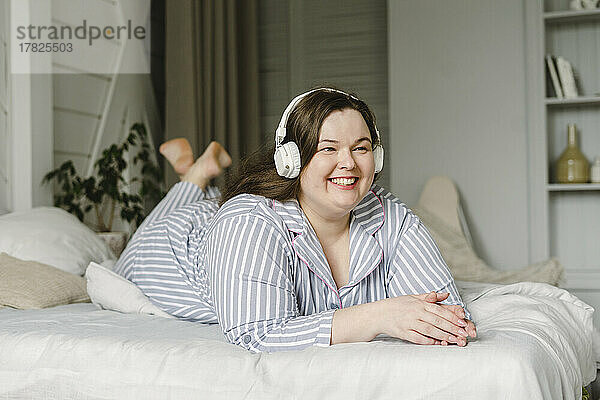 Glückliche Frau  die zu Hause im Bett liegt und Musik über kabellose Kopfhörer genießt