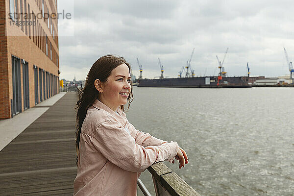 Glückliche junge Frau steht am Geländer im Hamburger Hafen