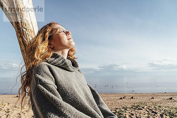 Frau genießt das Sonnenlicht und lehnt an einem Baum am Strand