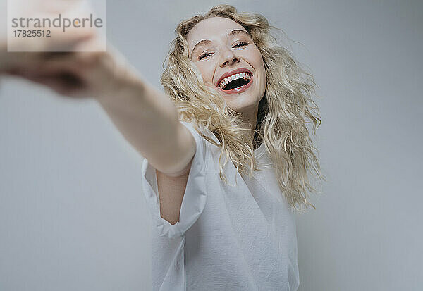 Blonde Frau lacht vor grauem Hintergrund