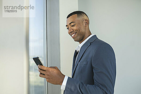 Lächelnder Geschäftsmann benutzt Smartphone im Büro
