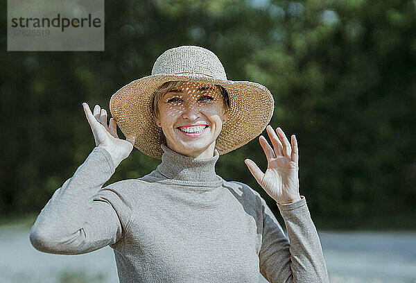 Lächelnde Frau mit Hut genießt den sonnigen Tag