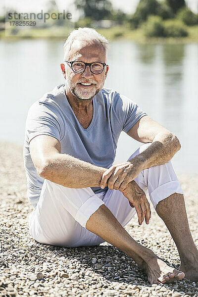 Lächelnder Mann mit Brille sitzt am Flussufer