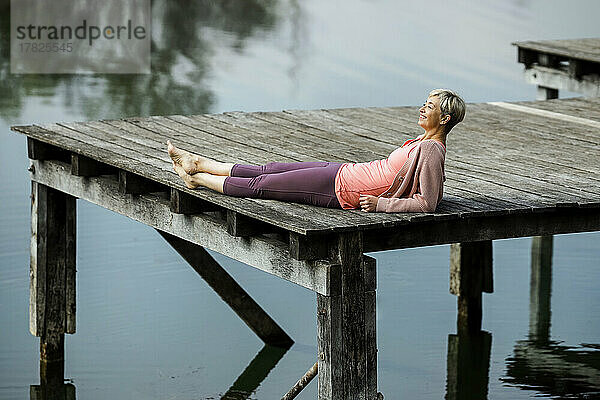 Lächelnde reife Frau liegt am Pier am See