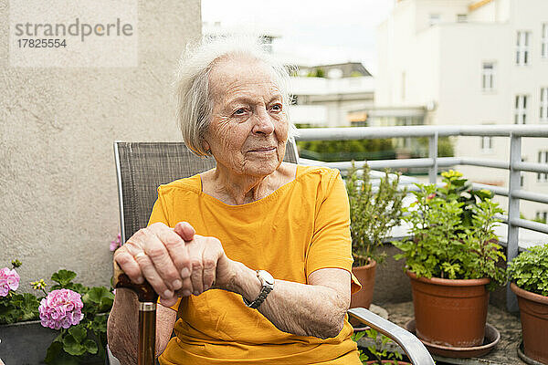Lächelnde ältere Frau mit Gehstock sitzt auf dem Balkon