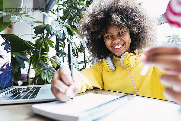 Lächelndes Mädchen macht Hausaufgaben am Laptop am Tisch im Café