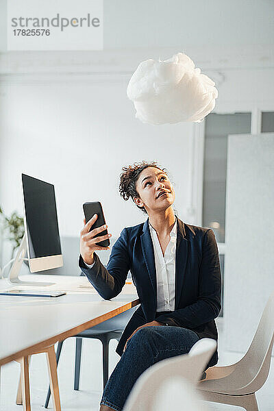 Junge Geschäftsfrau mit Smartphone blickt im Büro auf die Wolke