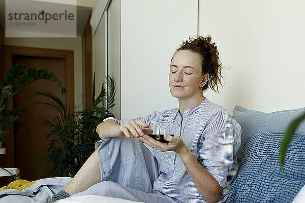Woman with eyes closed sitting with cup of tea at home
