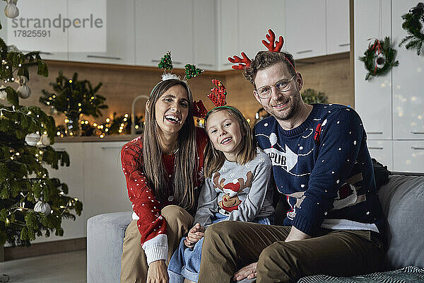 Glückliche Familie mit Weihnachtsgeweih sitzt zu Hause auf dem Sofa