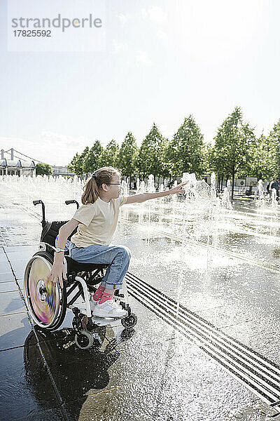 Mädchen sitzt im Rollstuhl und spielt mit Springbrunnen im Park