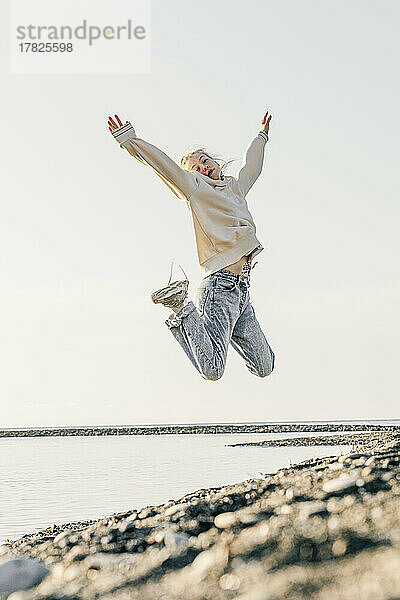Teenage girl with arms raised jumping at beach
