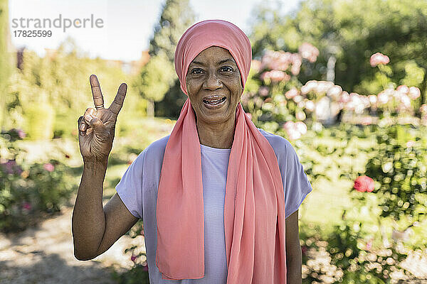 Glückliche Frau gestikuliert Friedenszeichen im öffentlichen Park