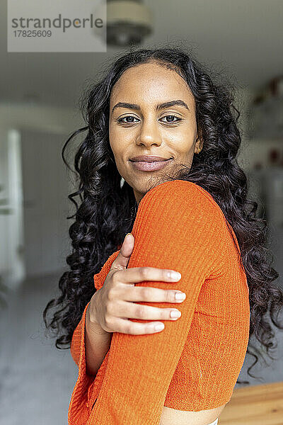 Glückliche Frau mit lockigem Haar  die zu Hause den Arm berührt