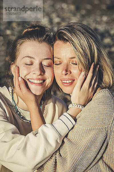 Smiling daughter and mother with eyes closed at beach