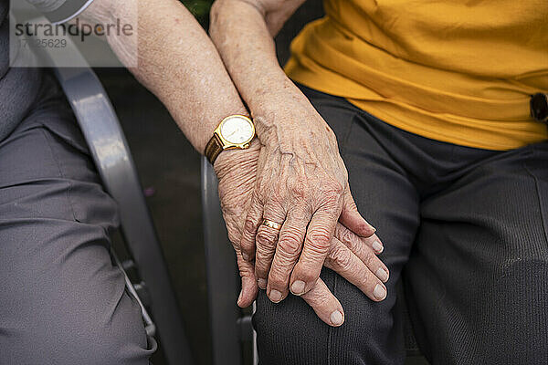 Hände eines älteren Mannes auf dem Schoß einer Frau