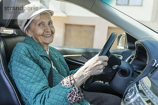 Lächelnde ältere Frau mit Baskenmütze sitzt im Auto